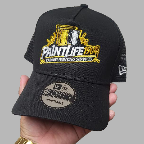 Black cap with 'PaintLife 1904' logo held by a hand against a gray background